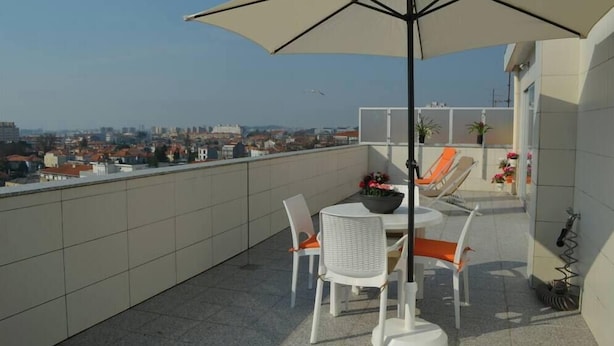 Een terras op het dak met een tafel, stoelen, een grote parasol en uitzicht over de stad.