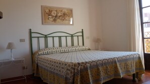 Una camera da letto con una struttura letto in metallo verde, copripiumino a motivi floreali, due lampade sui comodini e un quadro floreale appeso al muro.
