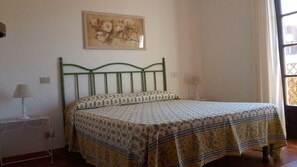 A bedroom with a green metal bed frame, floral-patterned bedspread, two bedside lamps, and a floral painting on the wall. - Holiday Homes La Pergola (Colle D'Orano)