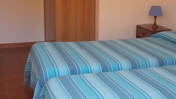 Ein Zimmer mit zwei Betten, einem Holzschrank, einem Nachttisch mit Lampe und einem gefliesten Boden.