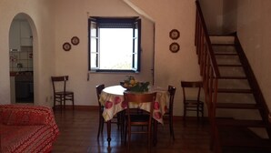 Un'area pranzo con un tavolo rotondo, sedie e una finestra con persiane. Si vede una scala sulla destra.