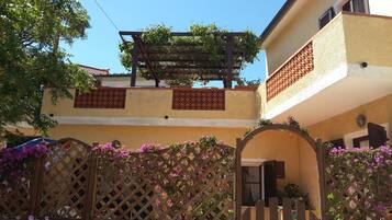 Un edificio residenziale con una pergola in legno, un cancello a traliccio e piante fiorite.