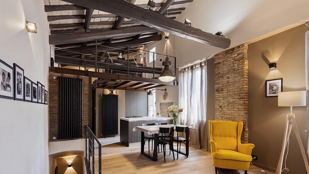 A modern interior with exposed wooden beams, a dining area with a table and chairs, a yellow armchair, and a kitchen in the background. - Beautifull loft in the hearth of Rome - A wonderful loft in the heart of Rome. (Roma)
