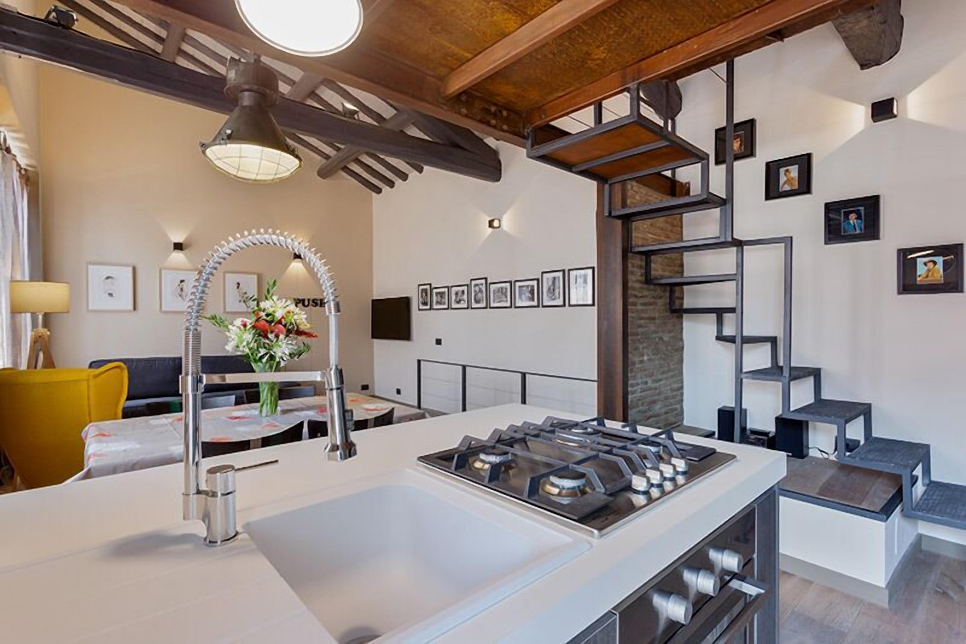 A modern kitchen with a central island, stainless steel appliances, and a dining area with a yellow chair.