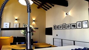 A modern dining area with a unique curved ceiling light fixture, a wooden dining table, and a wall adorned with framed photographs. - Beautifull loft in the hearth of Rome - A wonderful loft in the heart of Rome. (Roma)