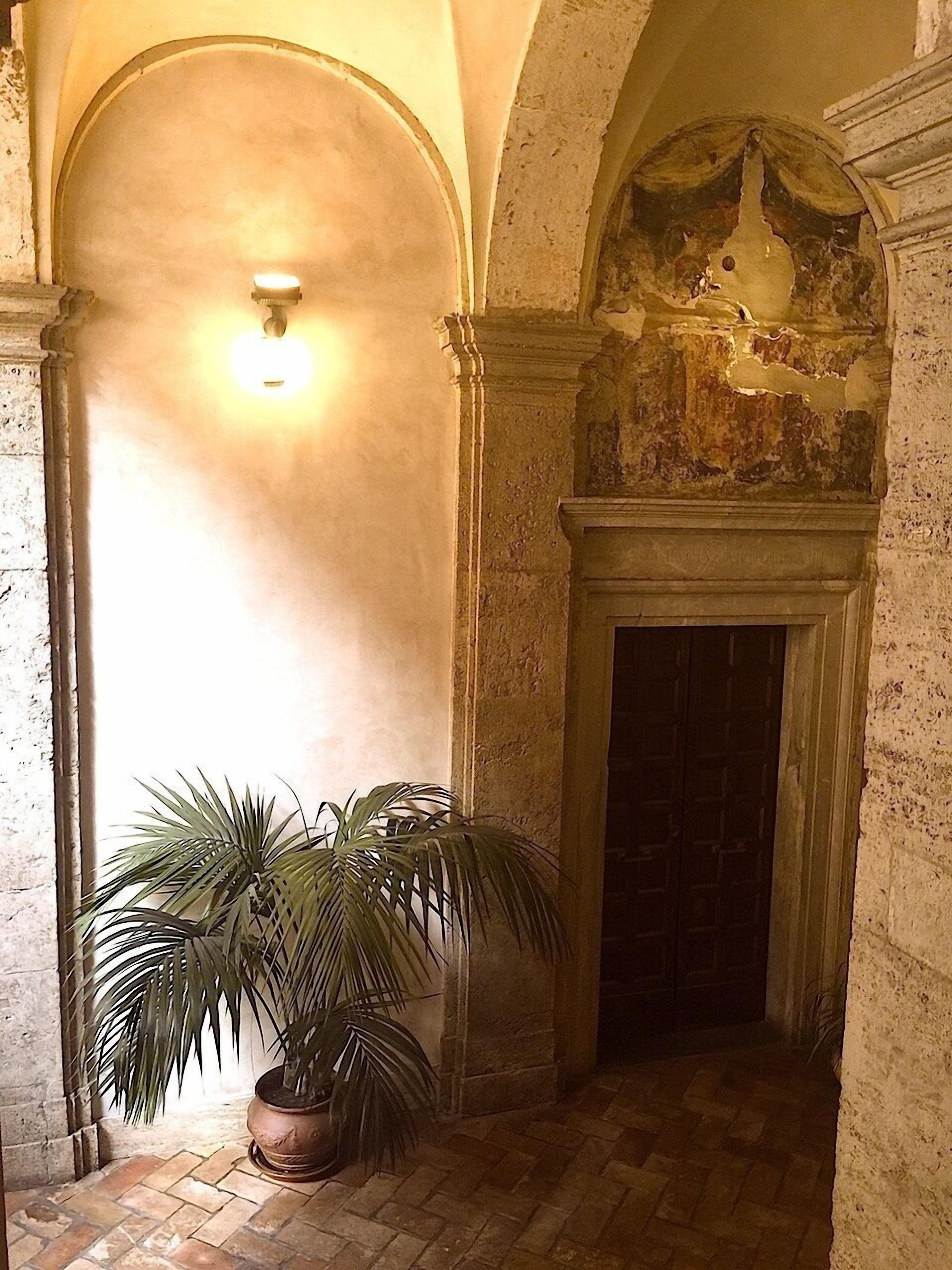 Un couloir doté d’un sol carrelé, d’un palmier en pot et d’une cheminée surmontée d’un plafond décoratif.