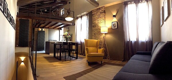A cozy living room with a sofa, a yellow armchair, a dining table with chairs, a kitchen area, and a staircase. - Beautifull loft in the hearth of Rome - A wonderful loft in the heart of Rome. (Roma)