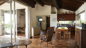 Amplia sala de estar con mesa de comedor, mecedora y cocina con armarios de madera y ventana con vista al jardín.