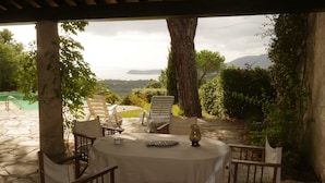 Un espacio de estar techado al aire libre con una mesa, sillas y vistas a una piscina y al paisaje.