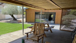 Eine Holzterrasse mit Tisch und Stühlen, einer darüberliegenden Pergola und Blick auf ein Haus mit Glastür.
