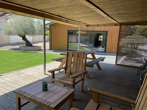 A wooden deck with a table and chairs, a pergola overhead, and a view of a house with a glass door. - At the heart of the Bassin d'Arcachon at LANTON near ANDERNOS (Lanton)
