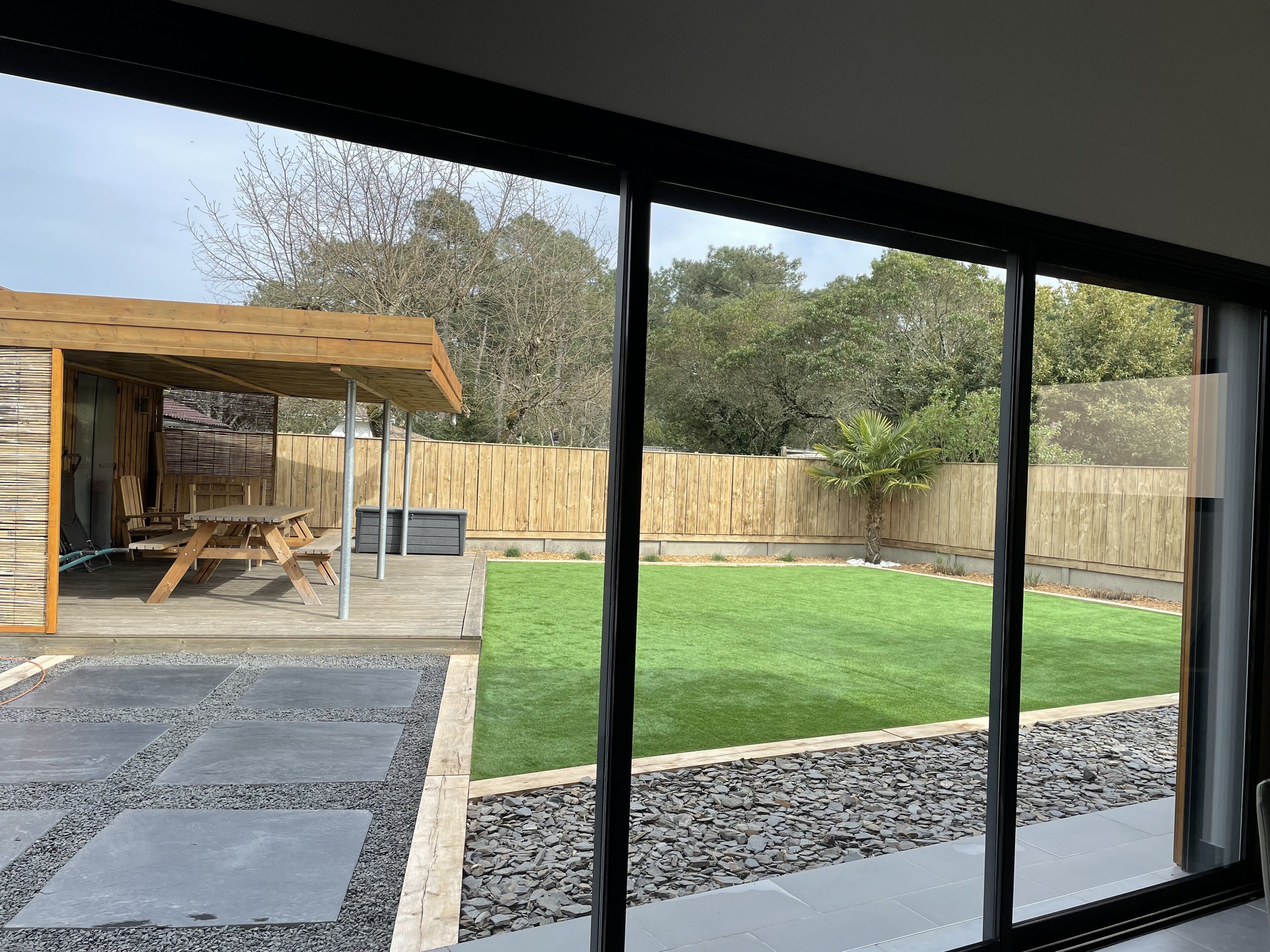 A modern outdoor patio with a wooden pergola, a seating area, and a well-maintained lawn.