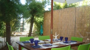Un espace de restauration en plein air avec une table en bois et des chaises vertes, entouré d’une clôture en bambou et d’arbres.