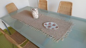 Une table à manger avec un plateau en verre, entourée de chaises en osier, et un set de table tissé agrémenté d’une assiette décorative.