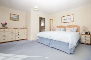 A bedroom with a large bed, a dresser, a nightstand, and a mirror.