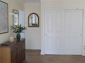 A hallway with a wooden dresser, a potted plant, a framed map, and a white door.