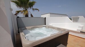 A hot tub on a rooftop terrace with a palm tree and a white building in the background.