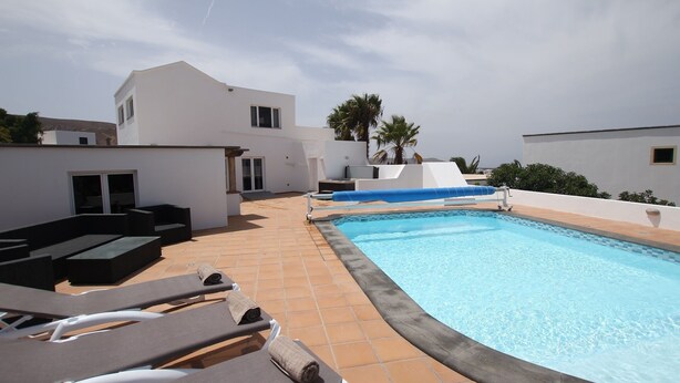 A rooftop pool area with lounge chairs, a blue slide, and a white building in the background.