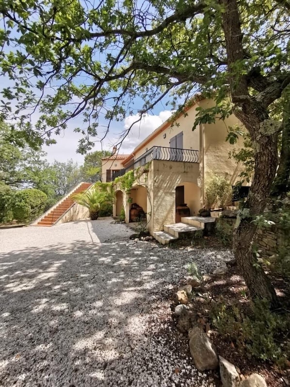 A house with a stone staircase leading to a covered porch, surrounded by trees and gravel.