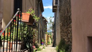 A narrow alleyway with buildings on either side, potted plants, and a clear blue sky. - Stylish villa, 13m private pool, tranquil garden, close to village amenities (Maureillas)
