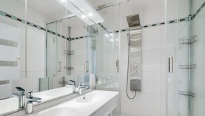 Een moderne badkamer met twee wastafels, een douche met glazen wanden en een grote spiegel.