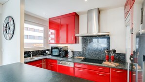 Een moderne keuken met rode kasten, een zwart aanrecht, een inbouwoven en een roestvrijstalen afzuigkap.