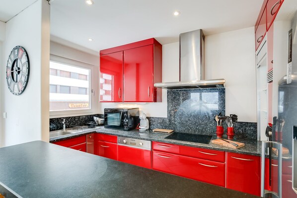 A modern kitchen with red cabinets, a black countertop, a built-in oven, and a stainless steel range hood. - Mountain type apartment 6-8 people at the foot of the slopes (Tignes)