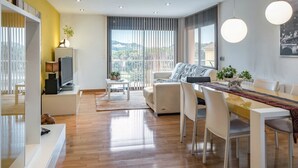 A modern living room with a sofa, dining table, and chairs, a TV, and a view of the outdoors.