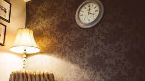 Ein Zimmer mit gestreiftem Wandteppich, einem Holzstuhl, einer Wanduhr und einer beleuchteten Lampe.