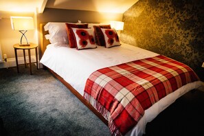 A neatly made bed with a red and white checkered blanket, two bedside lamps, and floral wallpaper.