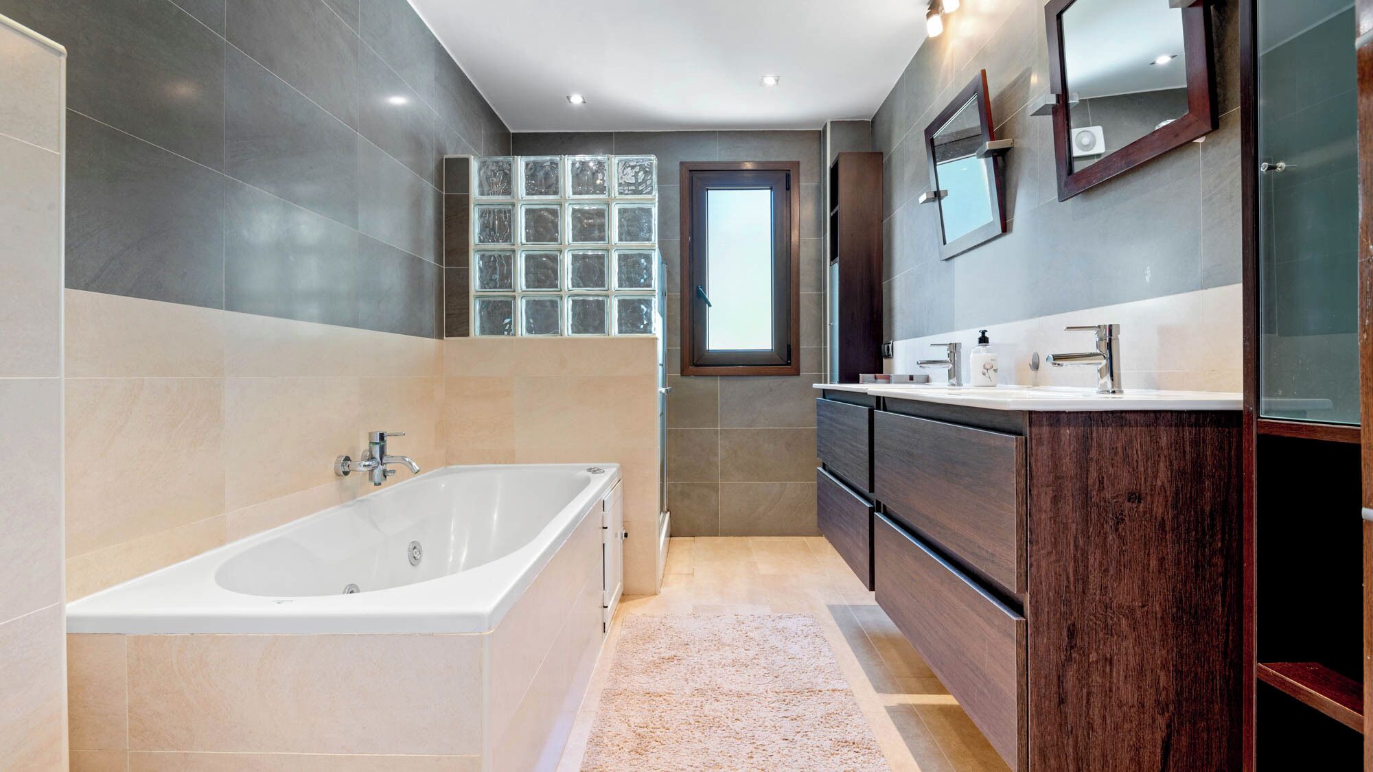 Une salle de bain moderne avec une baignoire sur pieds, un meuble-lavabo avec un miroir et une fenêtre laissant entrer la lumière naturelle.