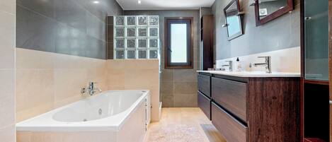 Une salle de bain moderne avec une baignoire sur pieds, un meuble-lavabo avec un miroir et une fenêtre laissant entrer la lumière naturelle.