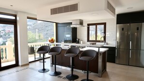 A modern kitchen with a central island, stainless steel appliances, and a view of the city. - Luxury modern villa with spectacular views of sea and heated private pool (La Herradura)