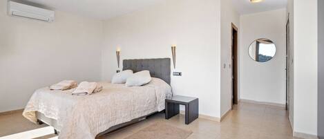 A bedroom with a bed, bedside table, wall-mounted lights, an air conditioner, and a mirror on the wall.