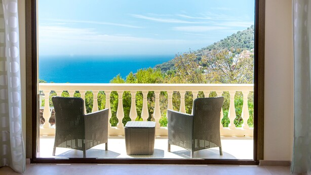 A balcony with wicker chairs and a small table, overlooking a coastal view with a clear sky and distant land. - Luxury modern villa with spectacular views of sea and heated private pool (La Herradura)