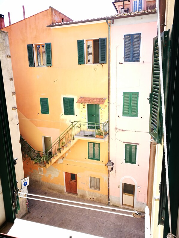 A multi-story building with balconies, green shutters, and a staircase leading to an upper floor.