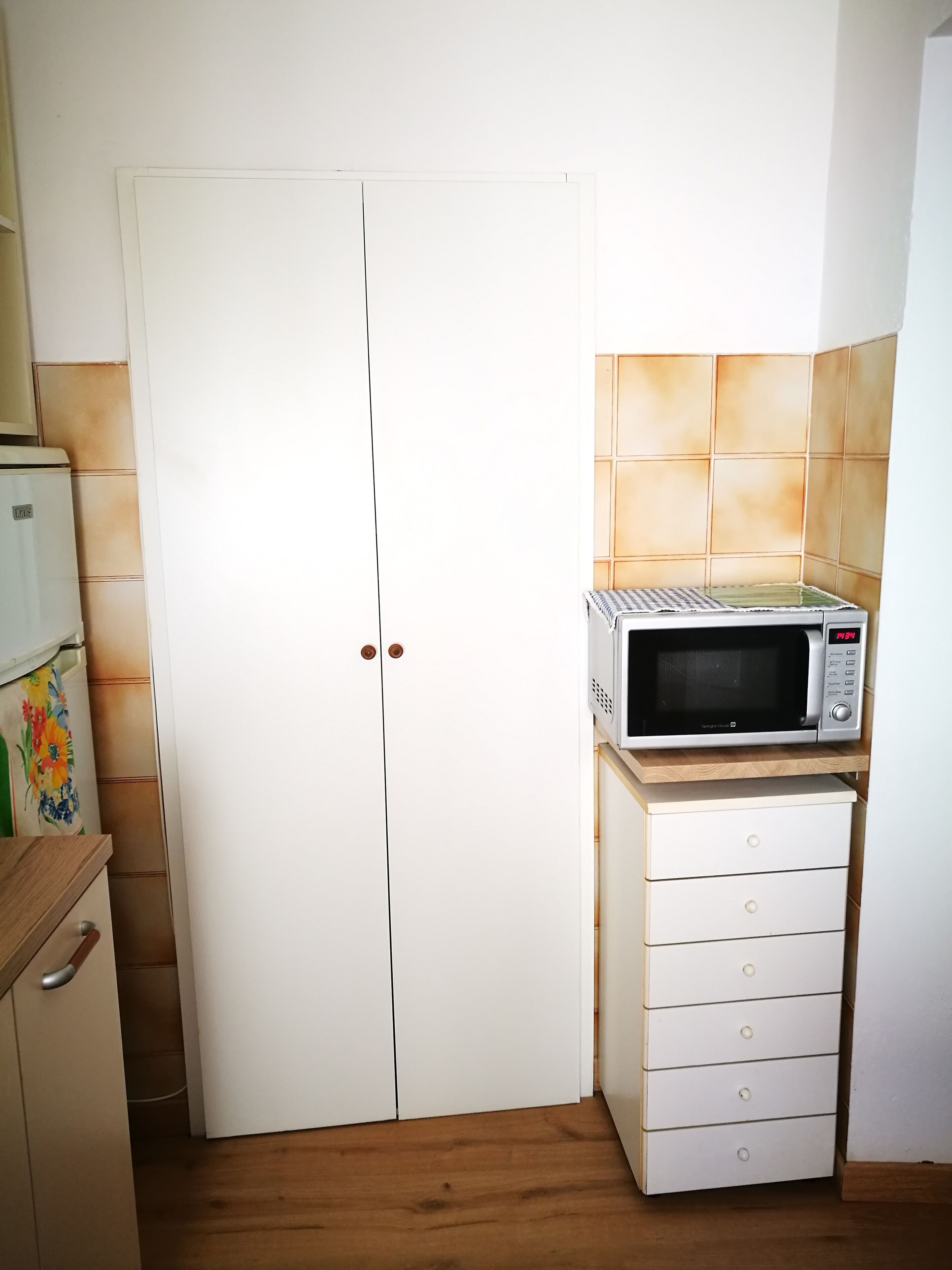 Une cuisine avec un réfrigérateur blanc, un four à micro-ondes posé sur une étagère en bois et un meuble blanc avec des tiroirs.