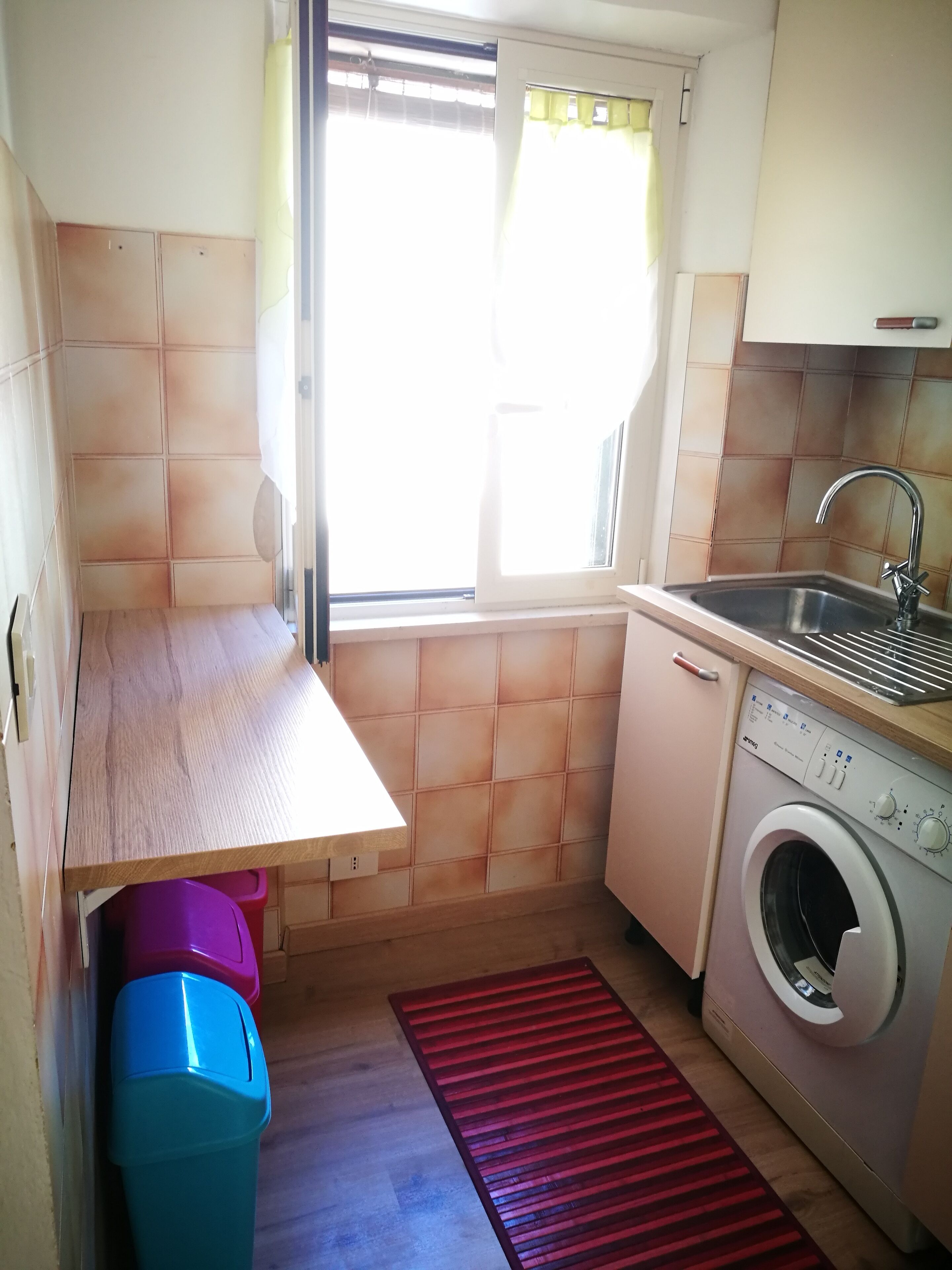 Una cocina compacta con lavadora, lavamanos y ventana con cortinas.