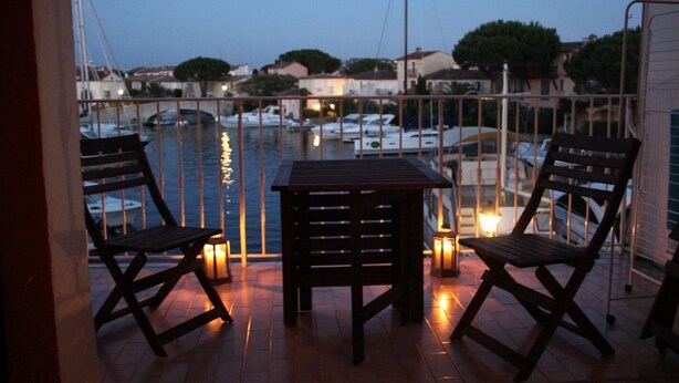 Une terrasse avec une table et deux chaises, donnant sur une marina où sont amarrés des bateaux.