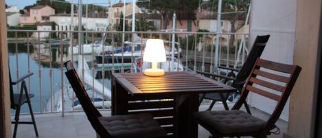 Un balcón con una mesa y dos sillas, con vistas a un puerto deportivo con barcos y edificios al fondo.