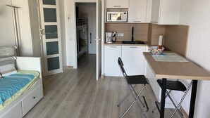 Une chambre de taille modeste comprenant un lit, un bureau avec une chaise, un four à micro-ondes et un coin cuisine.
