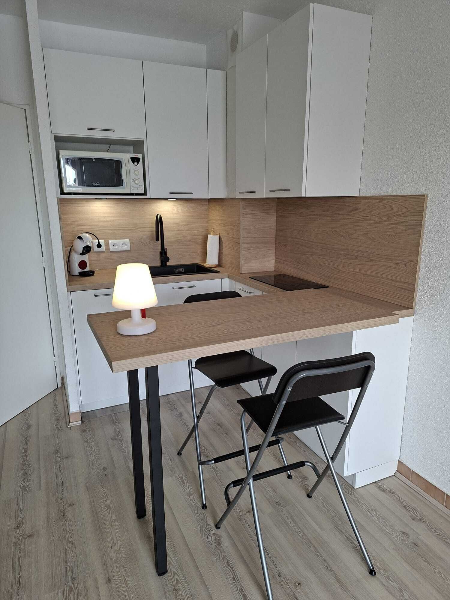 Una kitchenette compacta con microondas, pileta y una pequeña mesa con dos sillas.