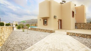 Una casa moderna con un vialetto in pietra che conduce a una porta, circondata da un'area ghiaiosa e una piscina.