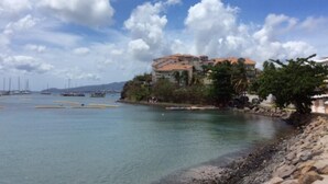 A coastal view with a building on a cliff overlooking the sea, boats in the water, and a clear sky. - T3 HOUSING WITH SEA VIEW AT POINTE DU BOUT (LES TROIS ILETS)
