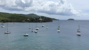 A coastal scene with multiple sailboats on calm waters, a green hillside with buildings, and a small island in the distance. - T3 HOUSING WITH SEA VIEW AT POINTE DU BOUT (LES TROIS ILETS)