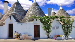 Une rangée de bâtiments traditionnels aux toits de pierre, aux murs blancs et aux portes en bois, sous un ciel bleu dégagé.