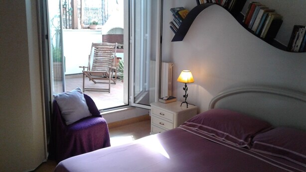 Une chambre avec deux lits, une table de chevet avec une lampe, une chaise et une vue sur le balcon extérieur.