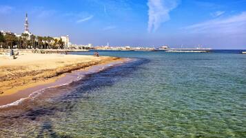 Una playa con agua cristalina, una orilla arenosa y edificios al fondo.