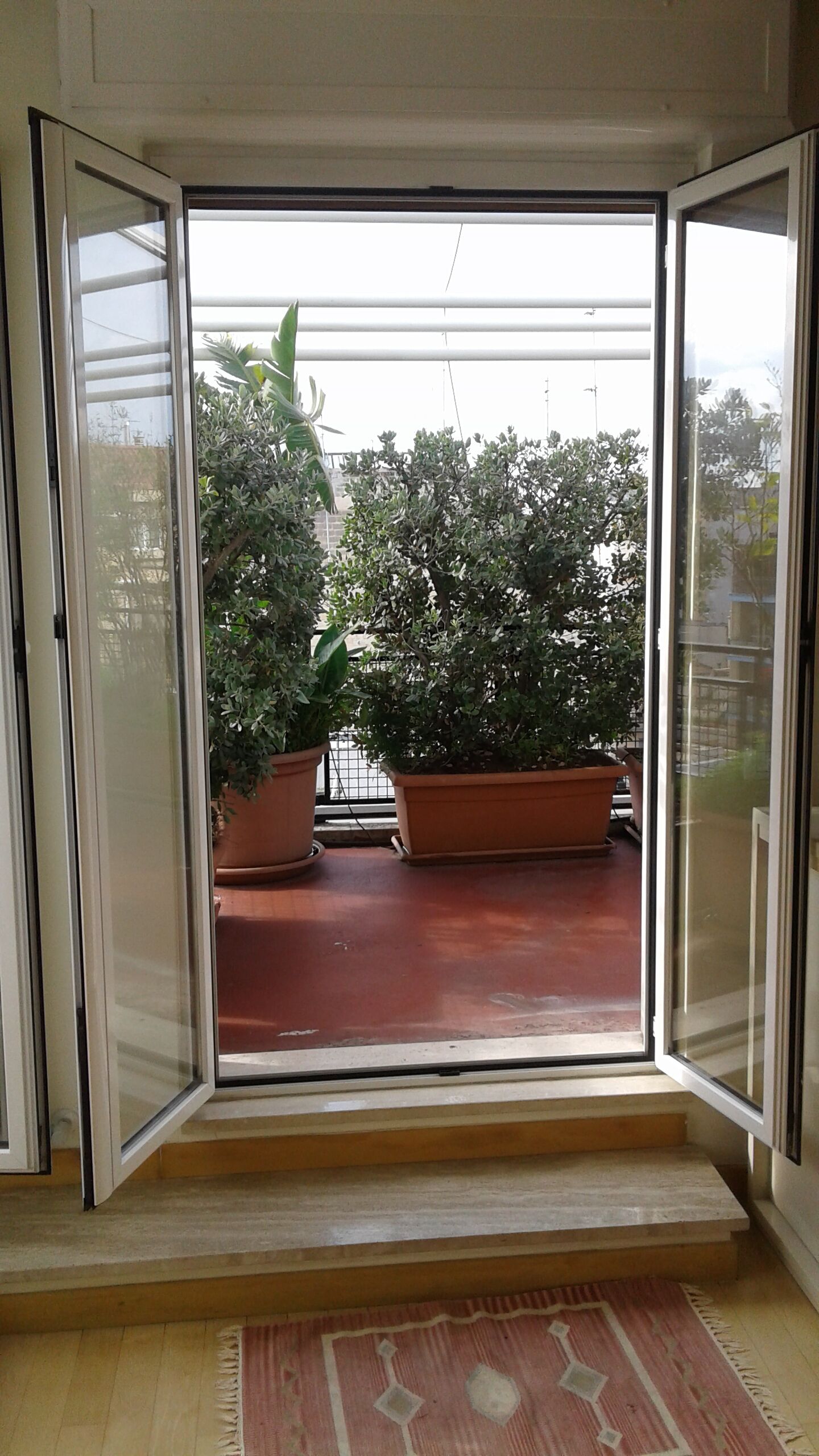 Una stanza con una porta scorrevole in vetro che dà su un balcone con piante in vaso.