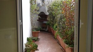 Une porte coulissante s’ouvre sur un patio carrelé agrémenté de plantes en pot et d’un barbecue.